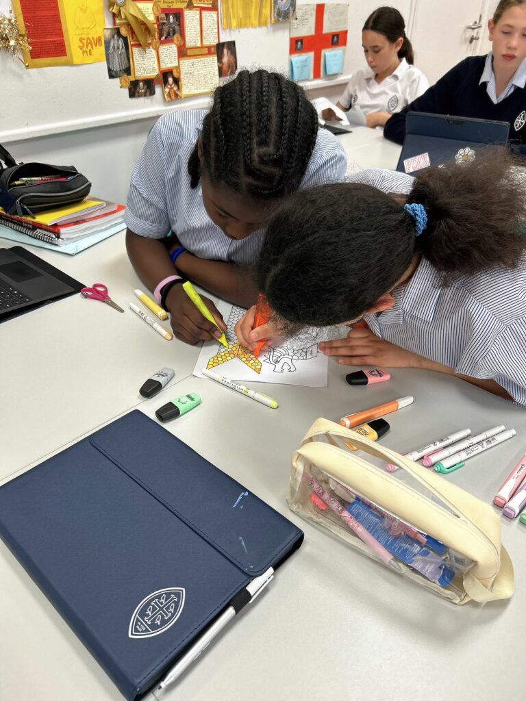 Two pupils colouring in their dragon boats. Pens are scattered across the table and each pupil has a laptop in front of them.