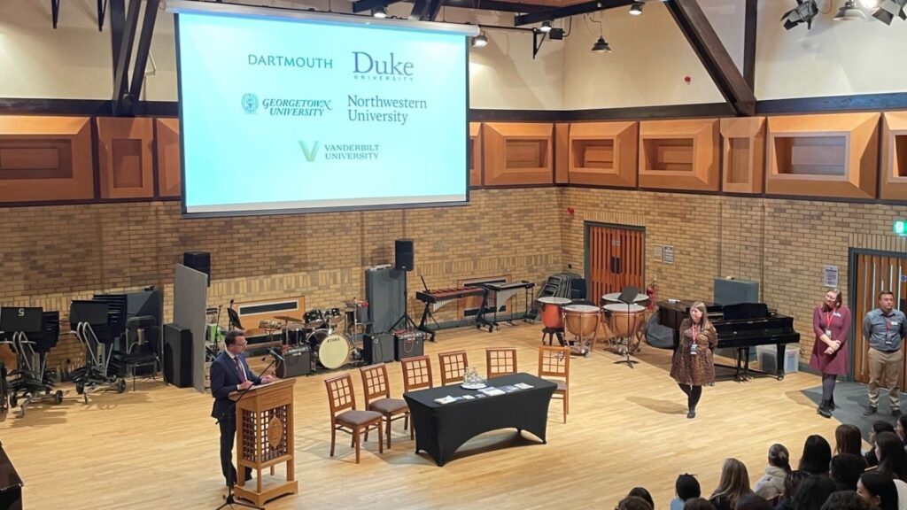 Mr Scupp stood at a lectern in front of a presentation showing popular US universities.