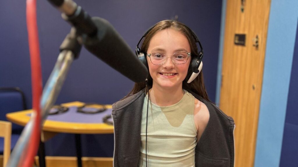Lilibet wearing headphones and smiling in front of the microphone.