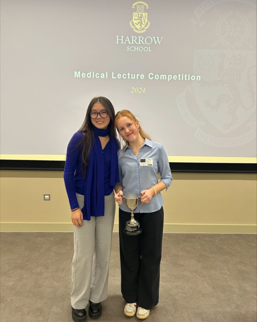 Astrid and Izzy stood together smiling. Izzy is holding her trophy.