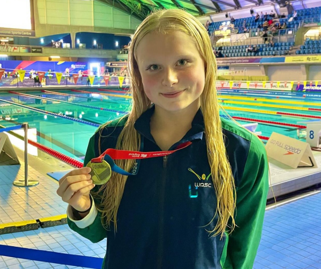Annabelle in front of the swimming pool, smiling with her medal.