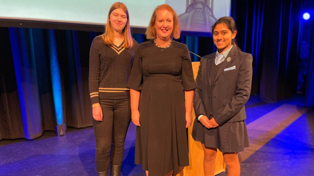 Victoria Prentis, stood on stage, between two Wycombe Abbey pupils.