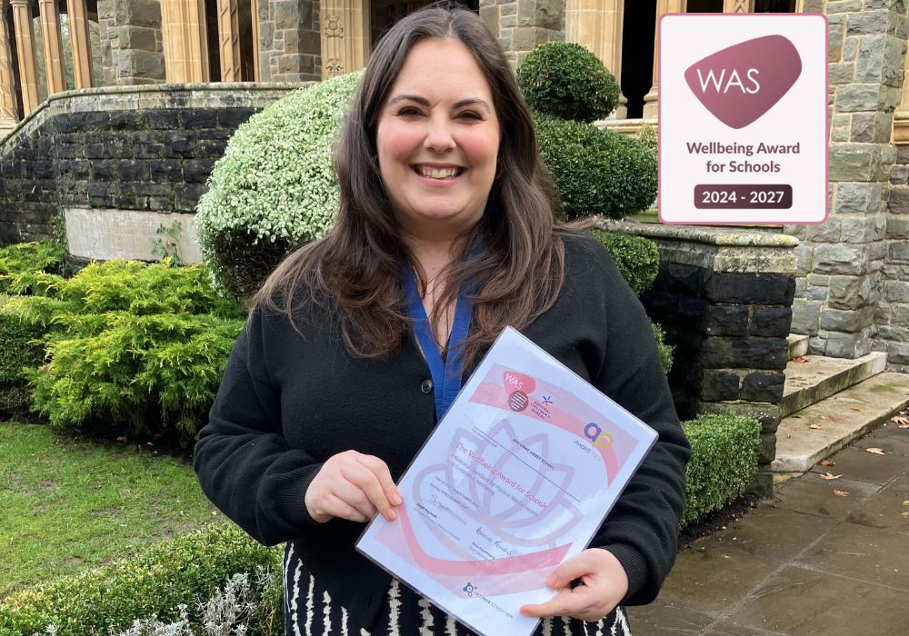Sophie Blunt stood in front of Chapel whilst holding the Wellbeing Award for Schools certificate.