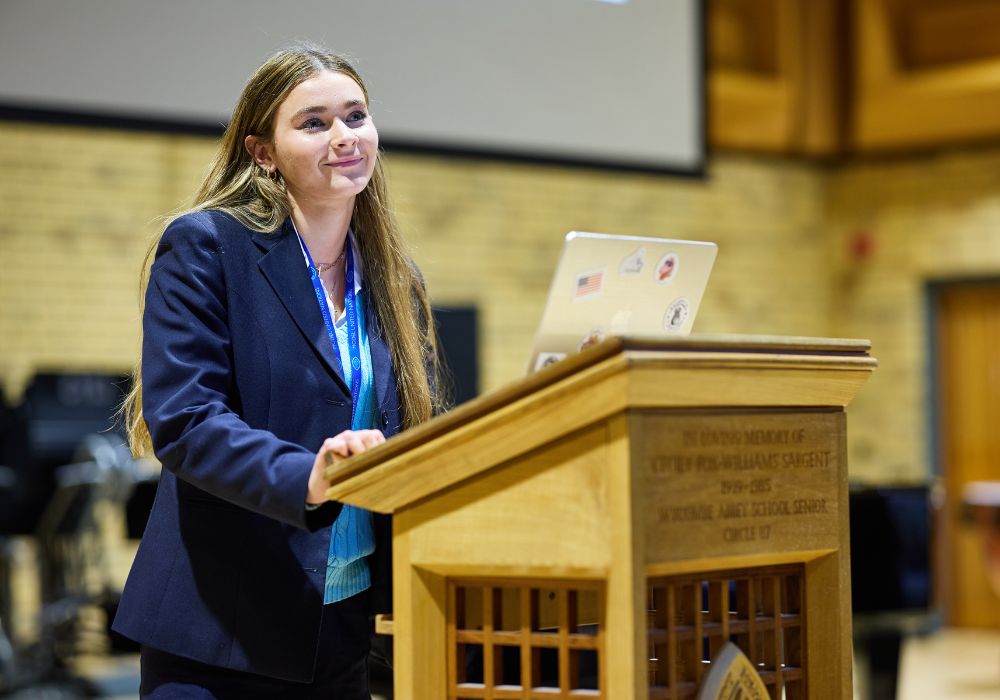 A pupils stood behind a wooden lectern.