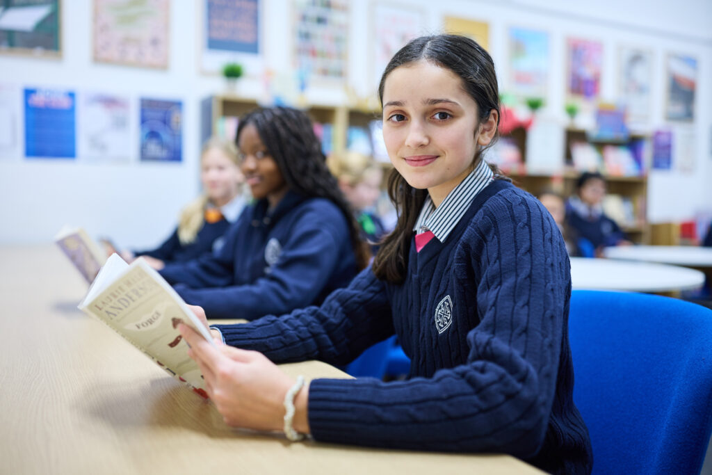 A girl holding an open book whilst smiling.
