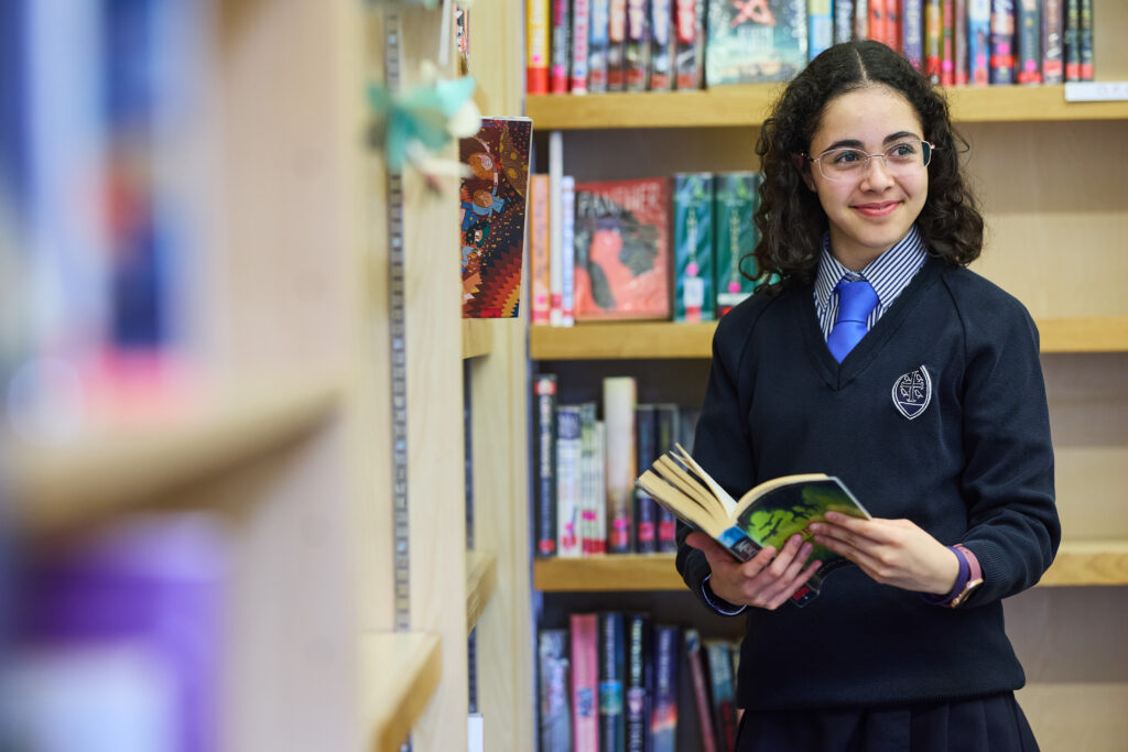 A girl holding an open book whilst smiling.