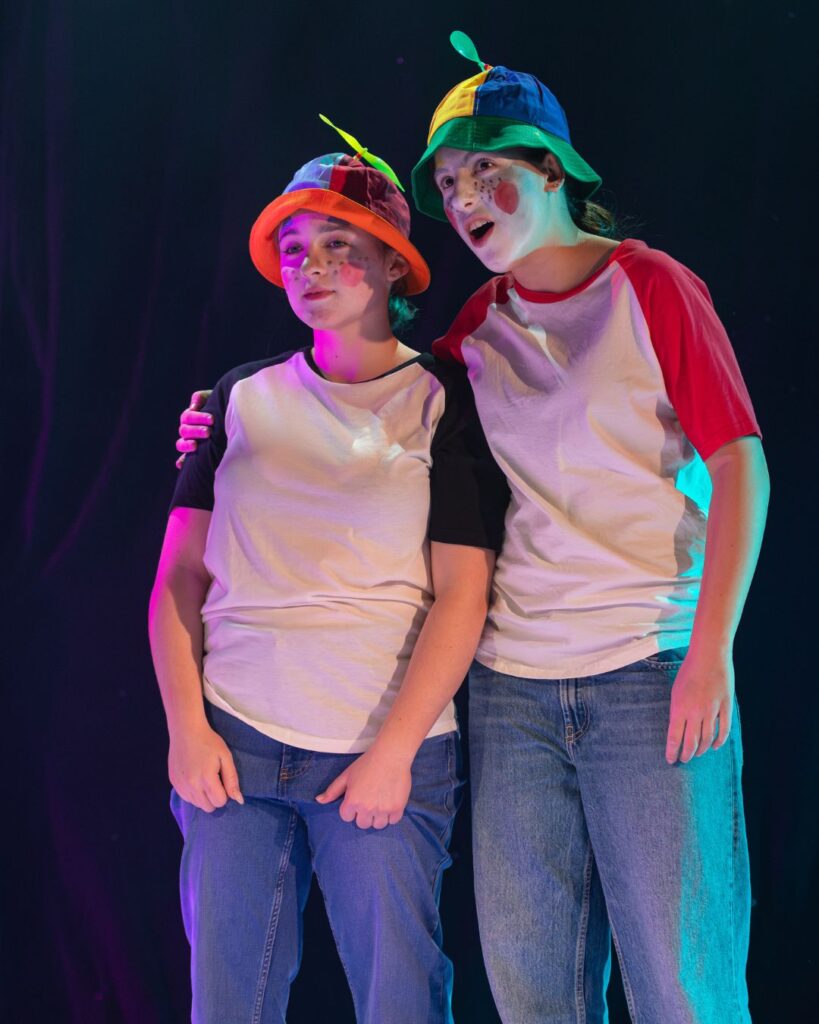 Two girls in jeans, a white t-shirt, and a multi-coloured bucket hat.