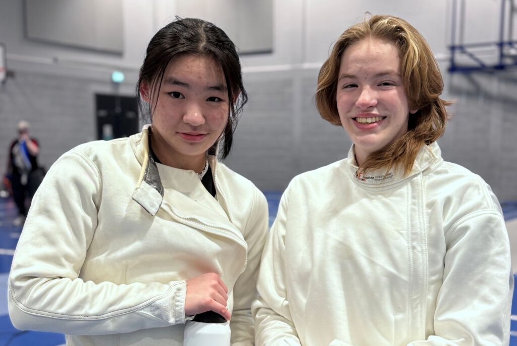 Abila and Nell smiling in a fencing lamé.