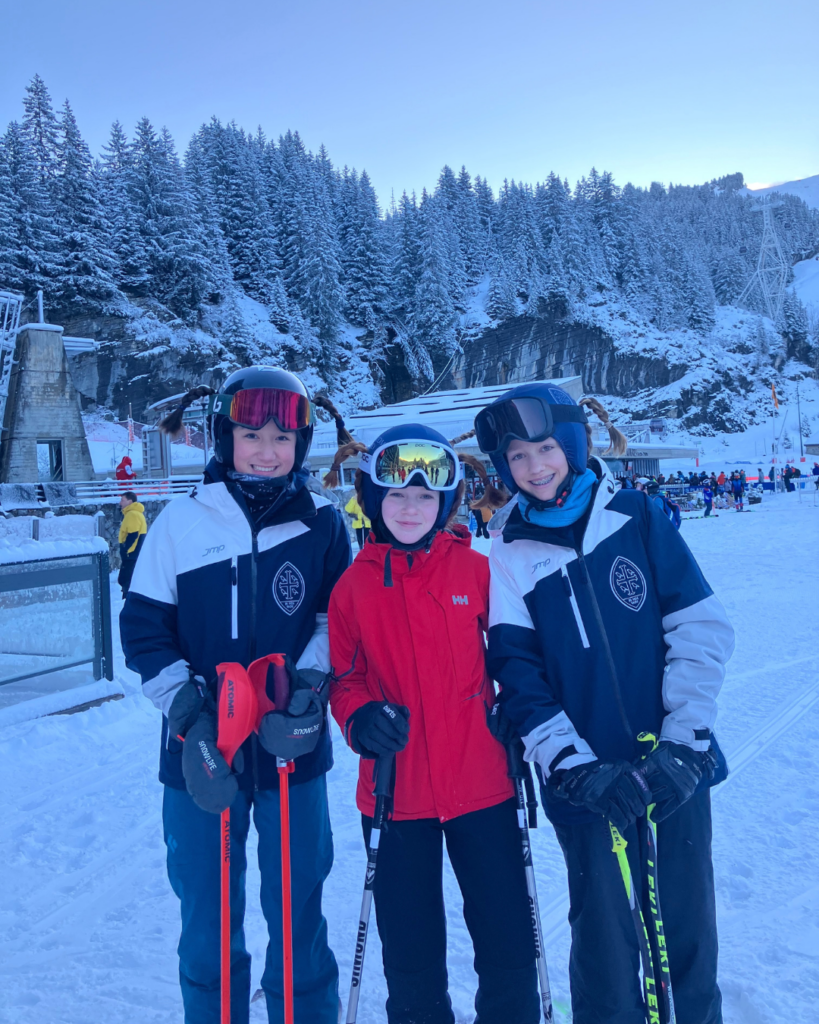 Three pupils in pigtail plaits smiling in ski gear.