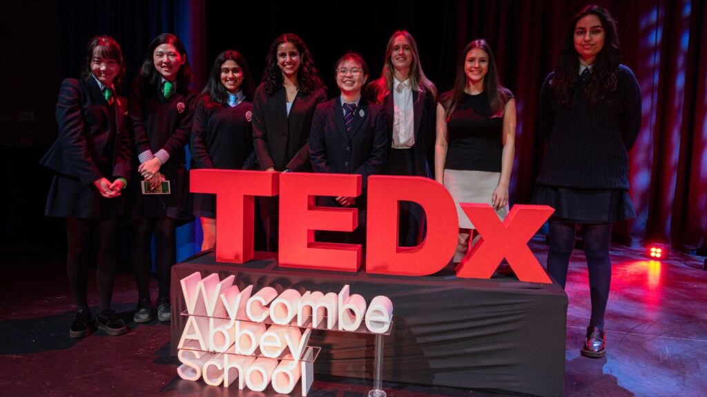 Wycombe Abbey pupils stood onstage, behind a red 'TEDx' sign and a white 'Wycombe Abbey School' sign.