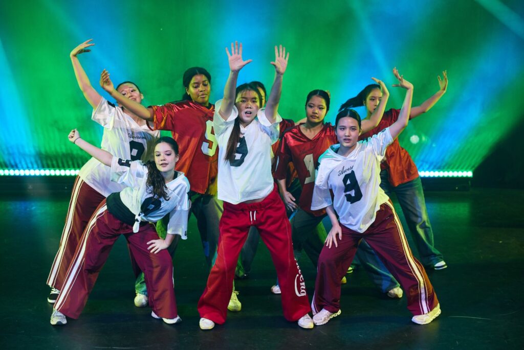 Pupils dancing on stage with white t-shirts and red trousers.