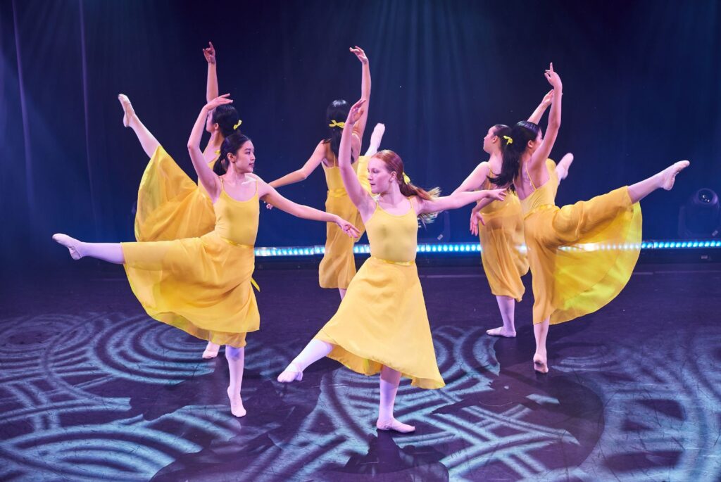 Pupils dancing on stage in yellow dresses.