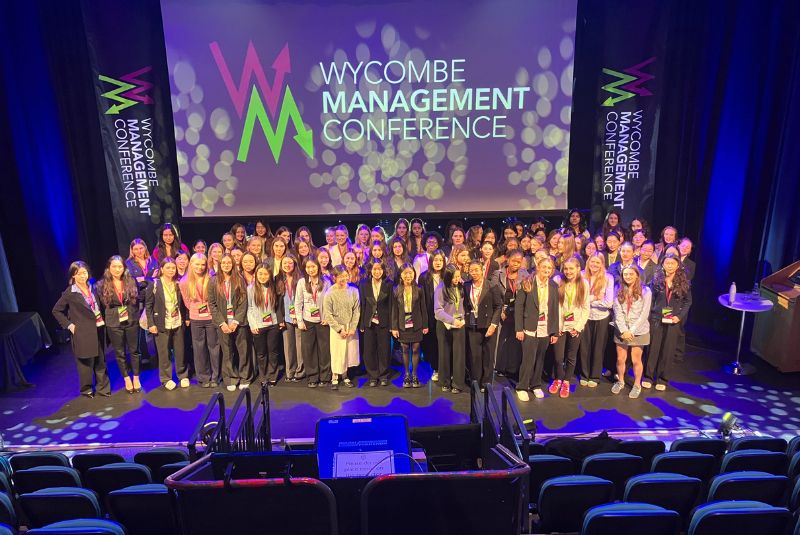 Wycombe Abbey Sixth Form stood on stage in front of a Wycombe Management Conference backdrop.