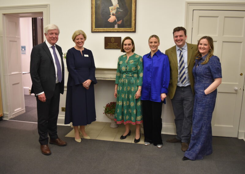 Lady Cynthia Hall, her family, and Jo Duncan stood below Lady Cynthia Hall's plaque and portrait.