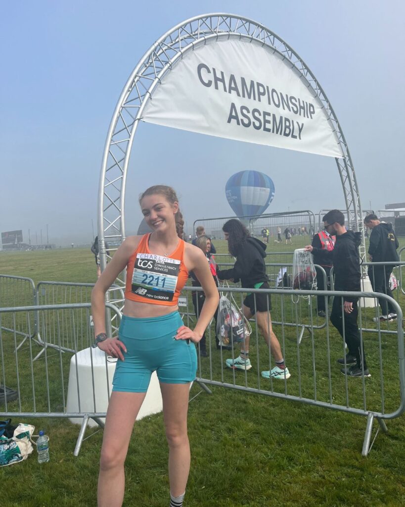 Charlotte posing with her hands on her hips in front of the Championship Assembly sign.