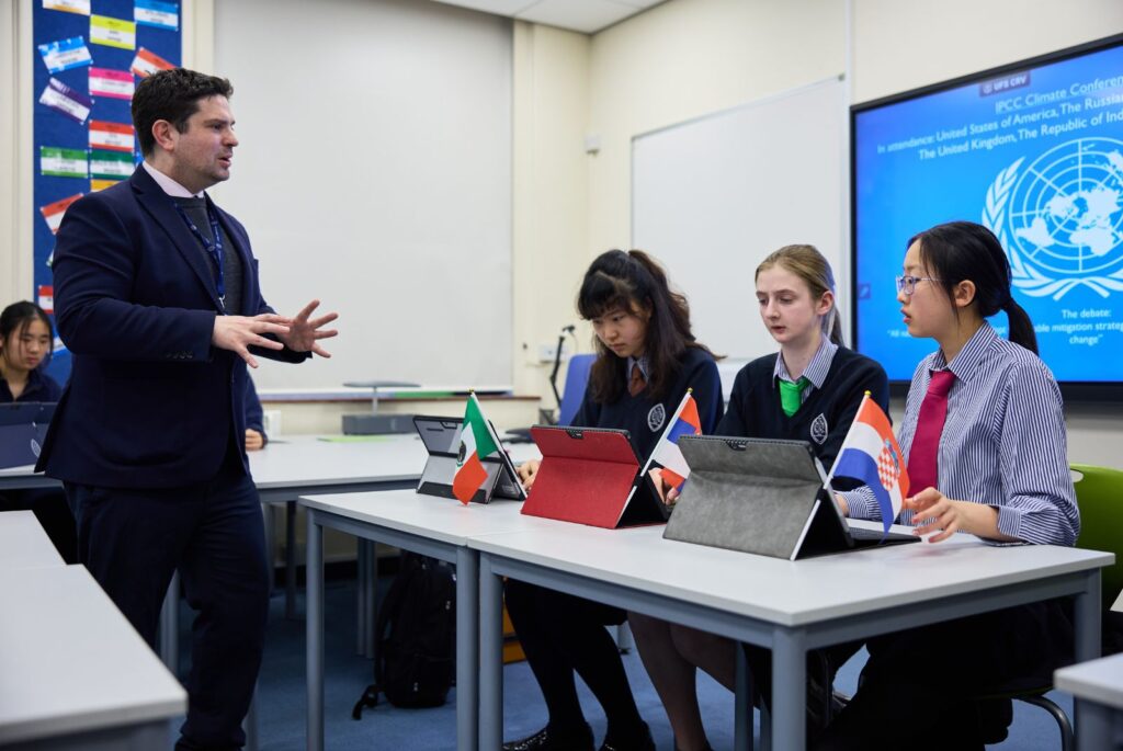 A teacher speaking to three pupils. A teacher speaking to three pupils. The pupils each have a country flag representing the country they are debating on behalf of.