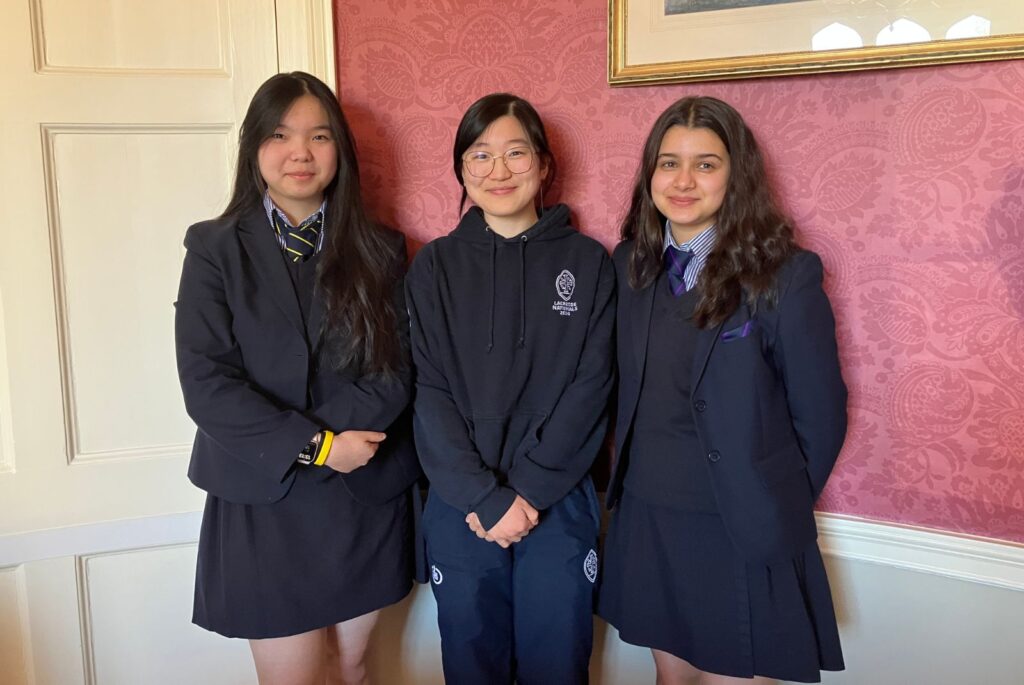 Dorian, Daphne and Fariha stood in front of a red wall.