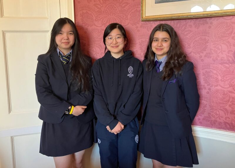 Dorian, Daphne and Fariha stood in front of a red wall.