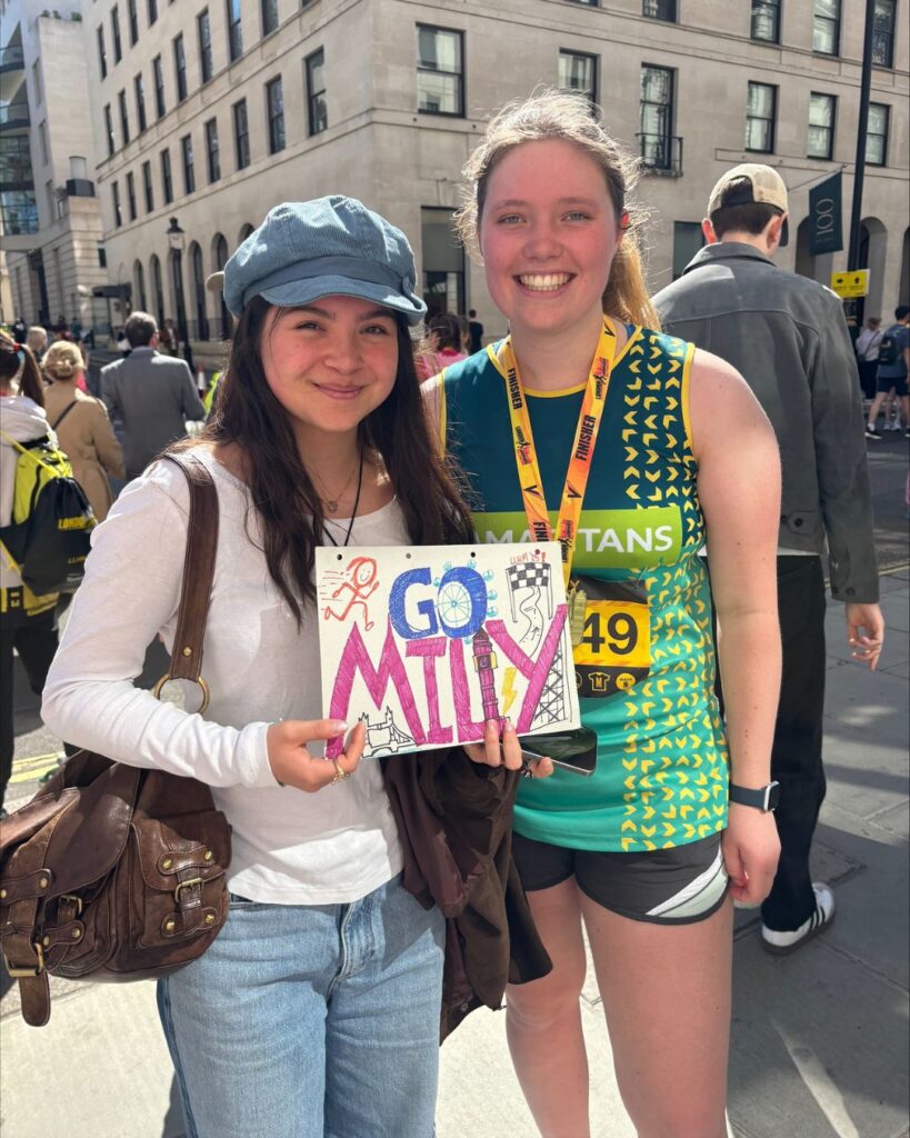 Milly stood to the right of her friend who is holding a 'Go Milly' sign.