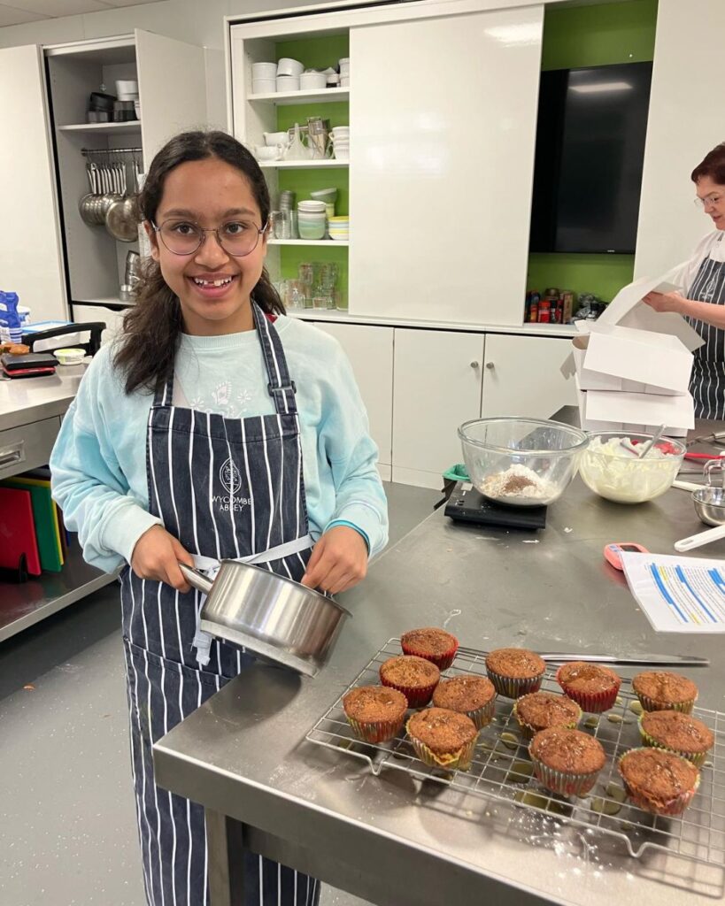A girl holding a saucepan whilst standing next to the cupcakes she made