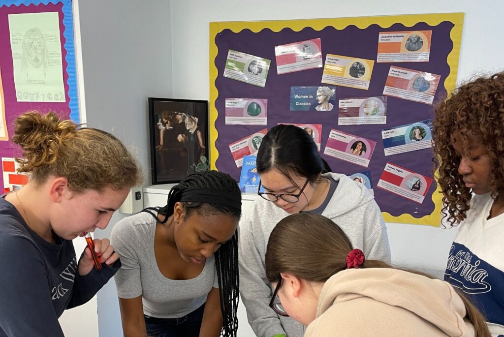 Girls crowding round a table whilst trying to solve a puzzle.