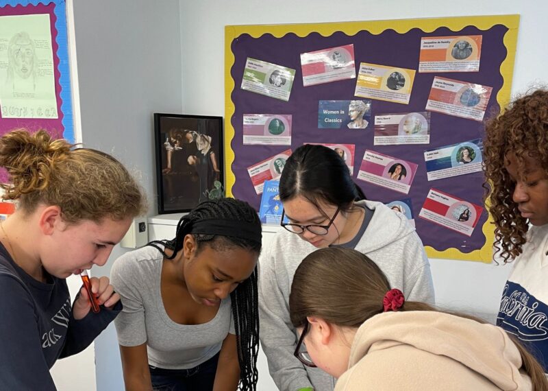 Girls gathered round a table whilst solving a puzzle.