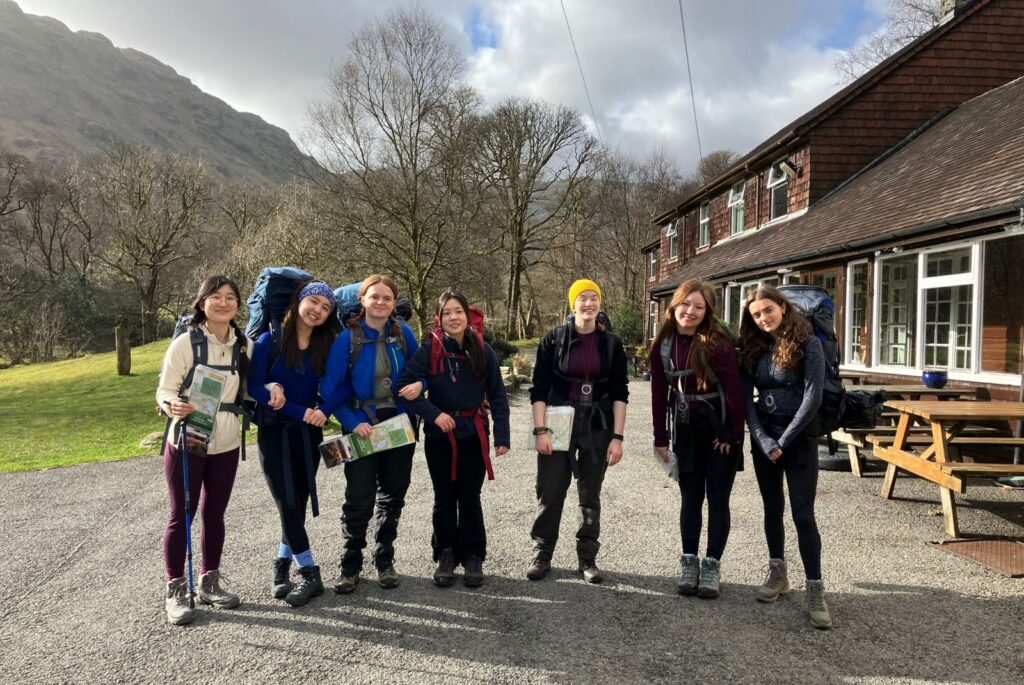 Pupils smiling with their maps and backpacks, stood at the bottom of a hill.