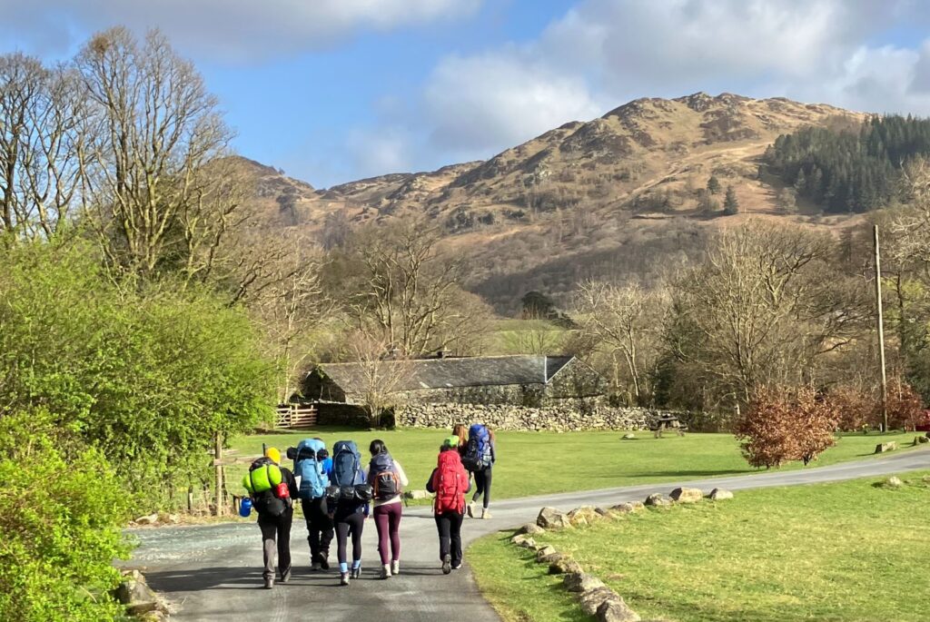 Pupils are walking along a country road with hills in the background.