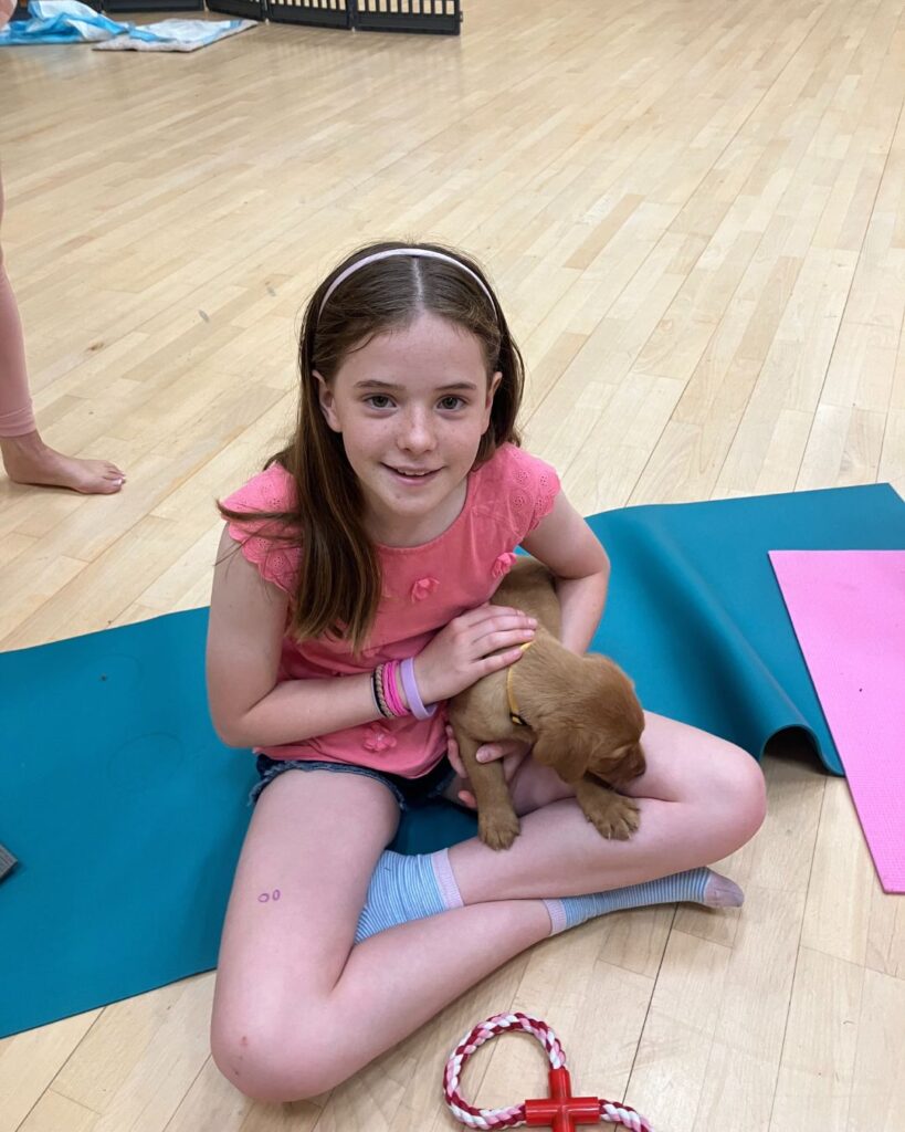 A girl sat on a yoga mat, with a fox-red labrador puppy on her lap.