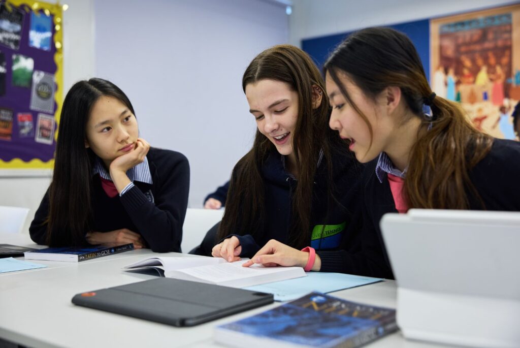 Three pupils sat in a classroom looking at a book.