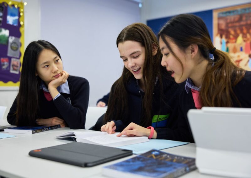 Three pupils sat in a classroom looking at a book.