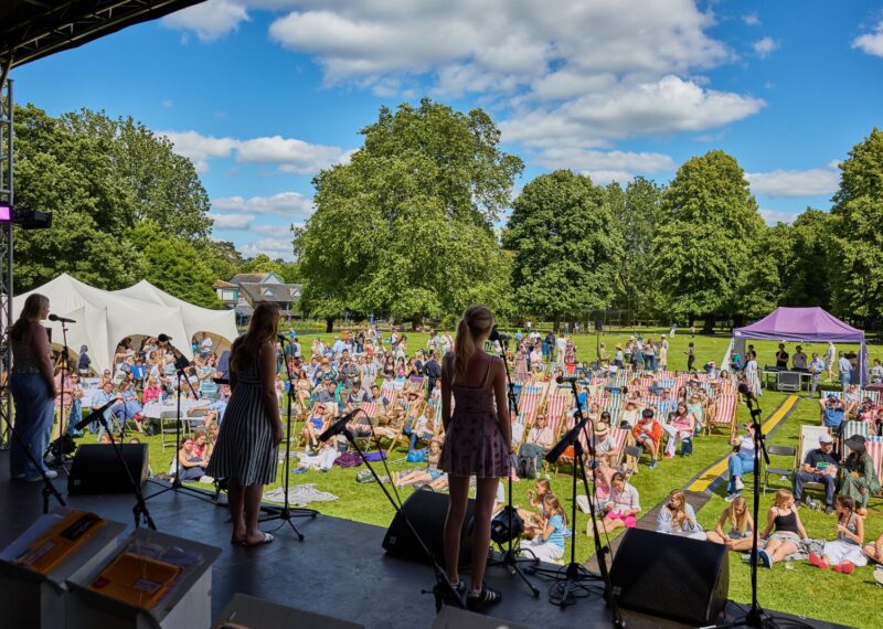 Three pupils stood on stage singing whilst looking out onto a busy crowd.