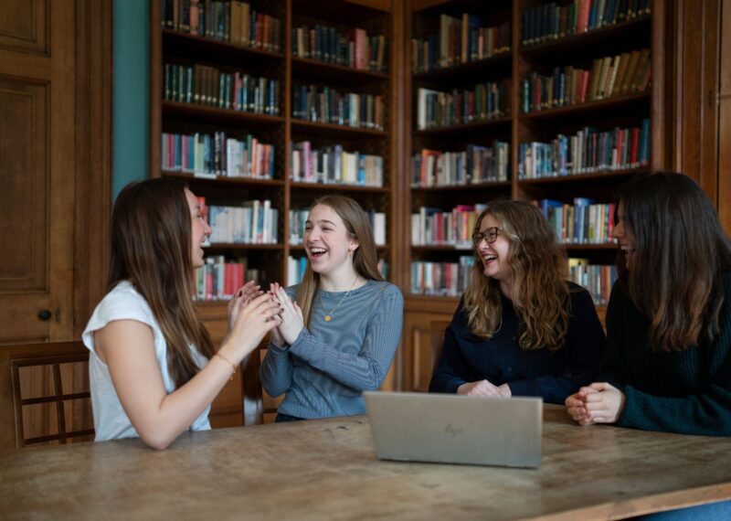 Pupils sat in a library whilst laughing with their teacher.
