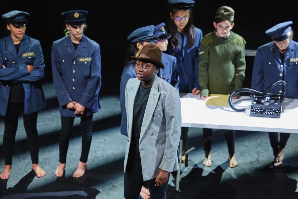 An UIII girl dressed in a blazer and cap stood in front of other pupils dressed in a US Navy costume.