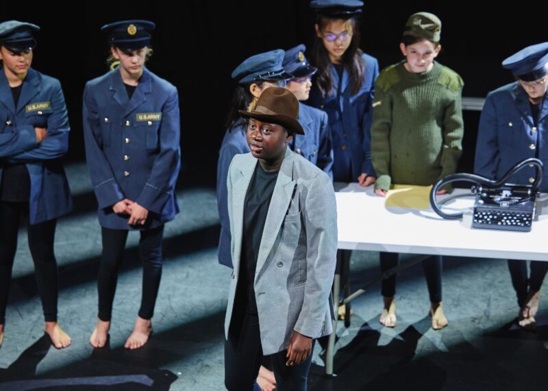 An UIII girl dressed in a blazer and cap stood in front of other pupils dressed in a US Navy costume.