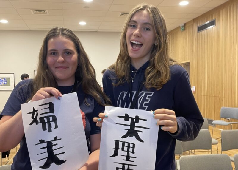 two girls holding pieces of paper with Japanese writing on it