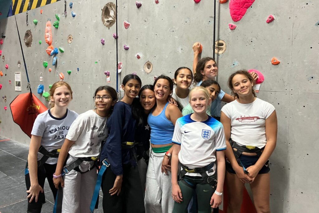 Girls stood together in front of a climbing wall.