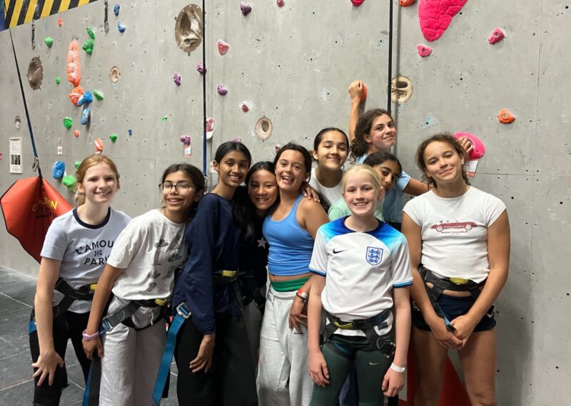 Girls stood together in front of a climbing wall.