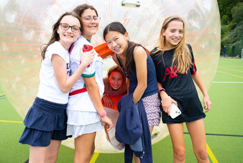 Four girls stood in front of a body zorb. Their friend is smiling behind them from inside the body zorb.