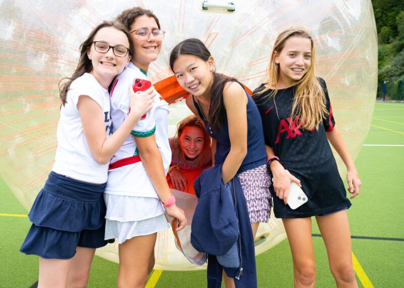 Four girls stood in front of a body zorb. Their friend is smiling behind them from inside the body zorb.
