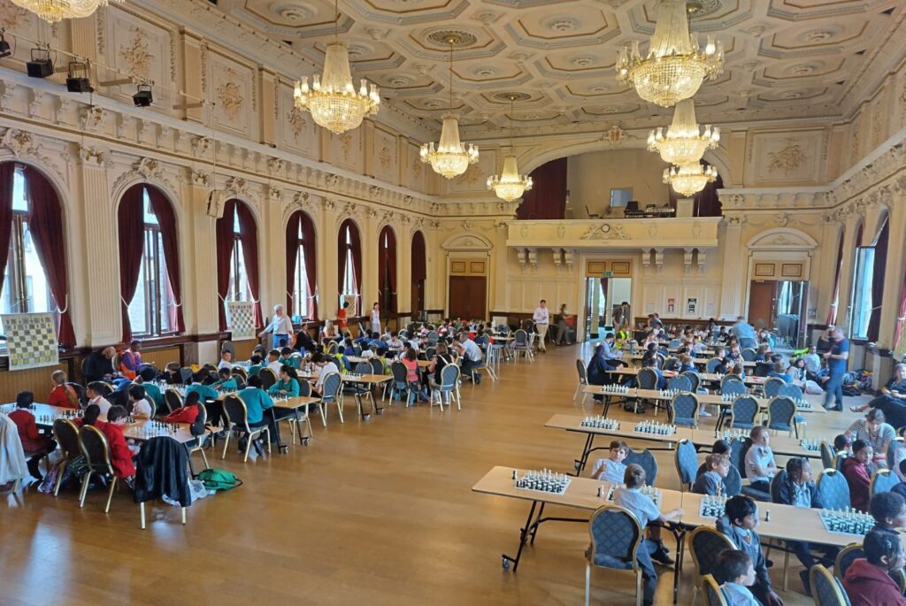 Young children sat in a hall playing chess.