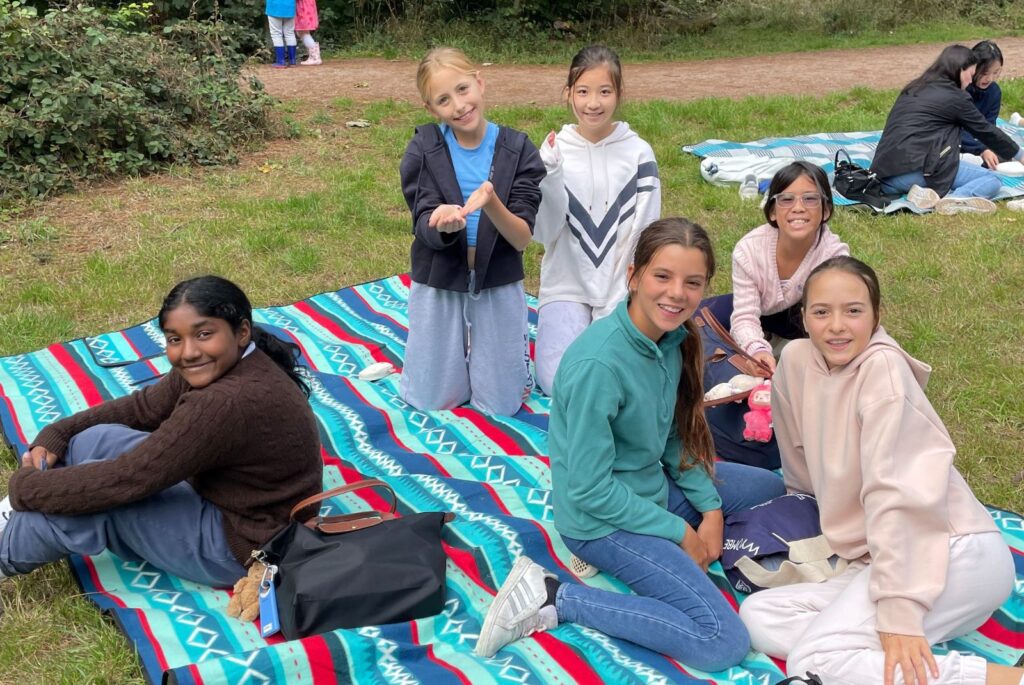 Six Wycombe Abbey pupils sat on a blue. red and navy picnic blanket.