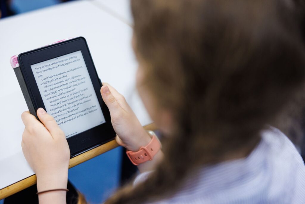 A girl sat at a desk reading her Kindle.