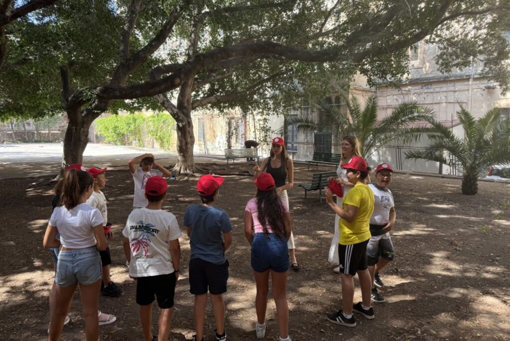 Mati and her friend stood in a courtyard talking to their students, who are standing in a circle.