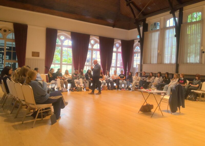 Andrew Wright stood in front of the UV who are sat in a semicircle.