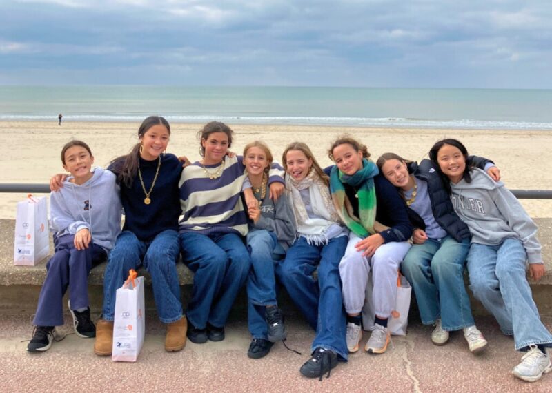 Girls all hugging in a line smiling at the camera on the beach