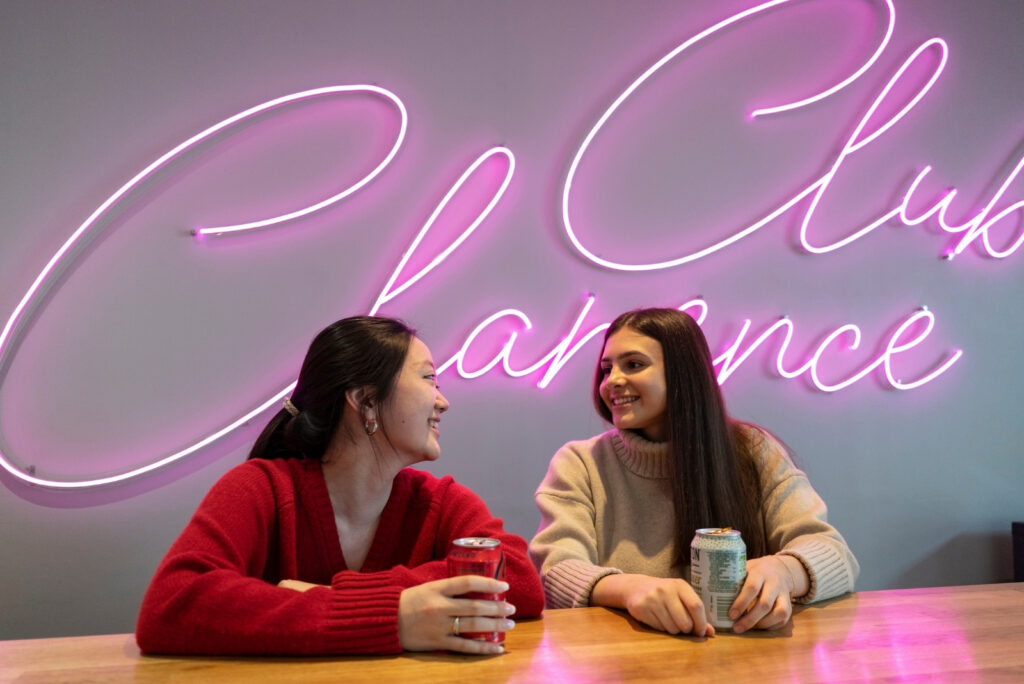 Two girls in front of a neon pink sign saying club clarence
