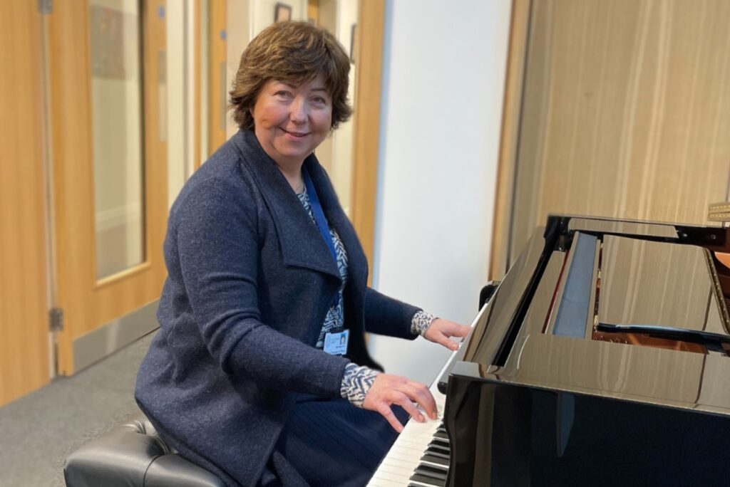 Women sitting at piano looking at the camera smiling with her fingers on the keys as if she were playing