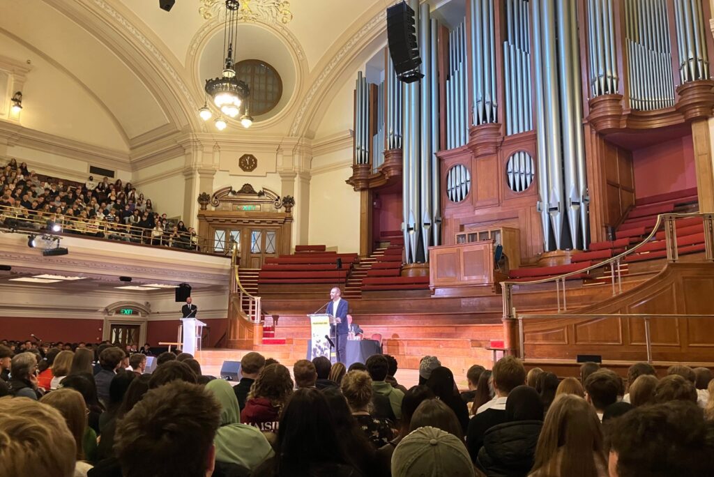 Big grand room with a male speaker on the stand talking into the mic