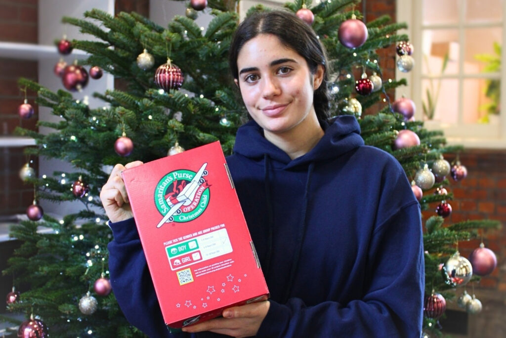 Girl holding her charity Christmas shoe box in front of a Christmas tree